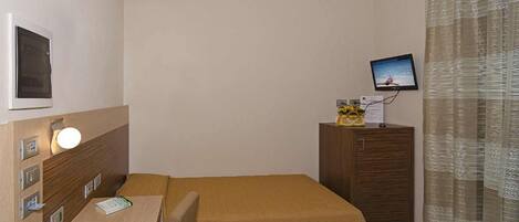 A hotel room with a bed, a desk with a computer, a television on a cabinet, and a curtain.