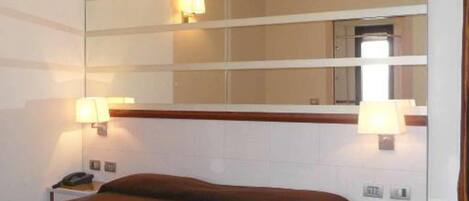 A hotel room with a large bed, bedside tables, a mirror, and a nightstand.