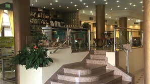 A lobby with a central staircase, a bar area, and a potted plant. - Hotel Eden (Viareggio)