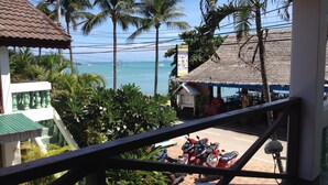 Vista desde un balcón sobre una playa con palmeras, un edificio de techo de paja y motocicletas estacionadas.