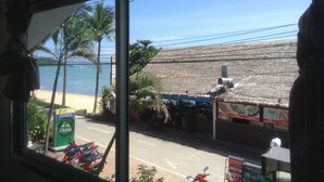 Vista de un restaurante frente a la playa con techo de paja, palmeras y un cielo azul despejado.