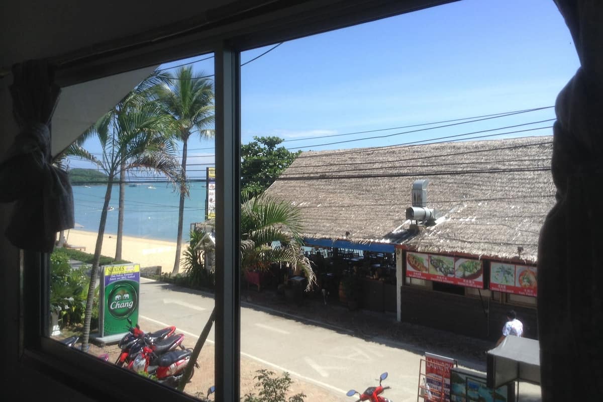 Vista de un restaurante frente a la playa con techo de paja, palmeras y un cielo azul despejado.