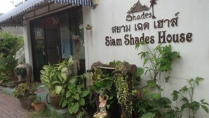 Un edificio con un letrero que dice "Shades Siam Shades House" y una estatua de una mujer con traje tradicional.