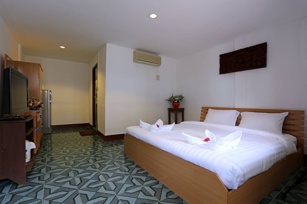 Habitación de hotel con cama, televisor, una mesita con una planta y piso estampado.