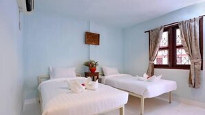 Una habitación de hotel con dos camas individuales, una mesita con un jarrón y una ventana con cortinas.