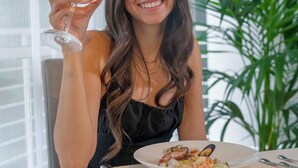 Una persona sentada a una mesa con un plato de comida y una copa de vino.