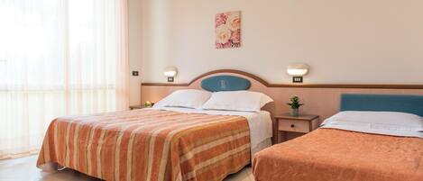 A hotel room with two beds, a nightstand with a lamp, a wall-mounted artwork, and a window with sheer curtains.