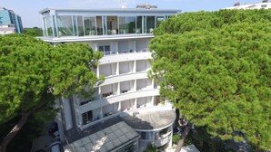 Un edificio de varios pisos con fachada de vidrio, rodeado de frondosos árboles verdes.
