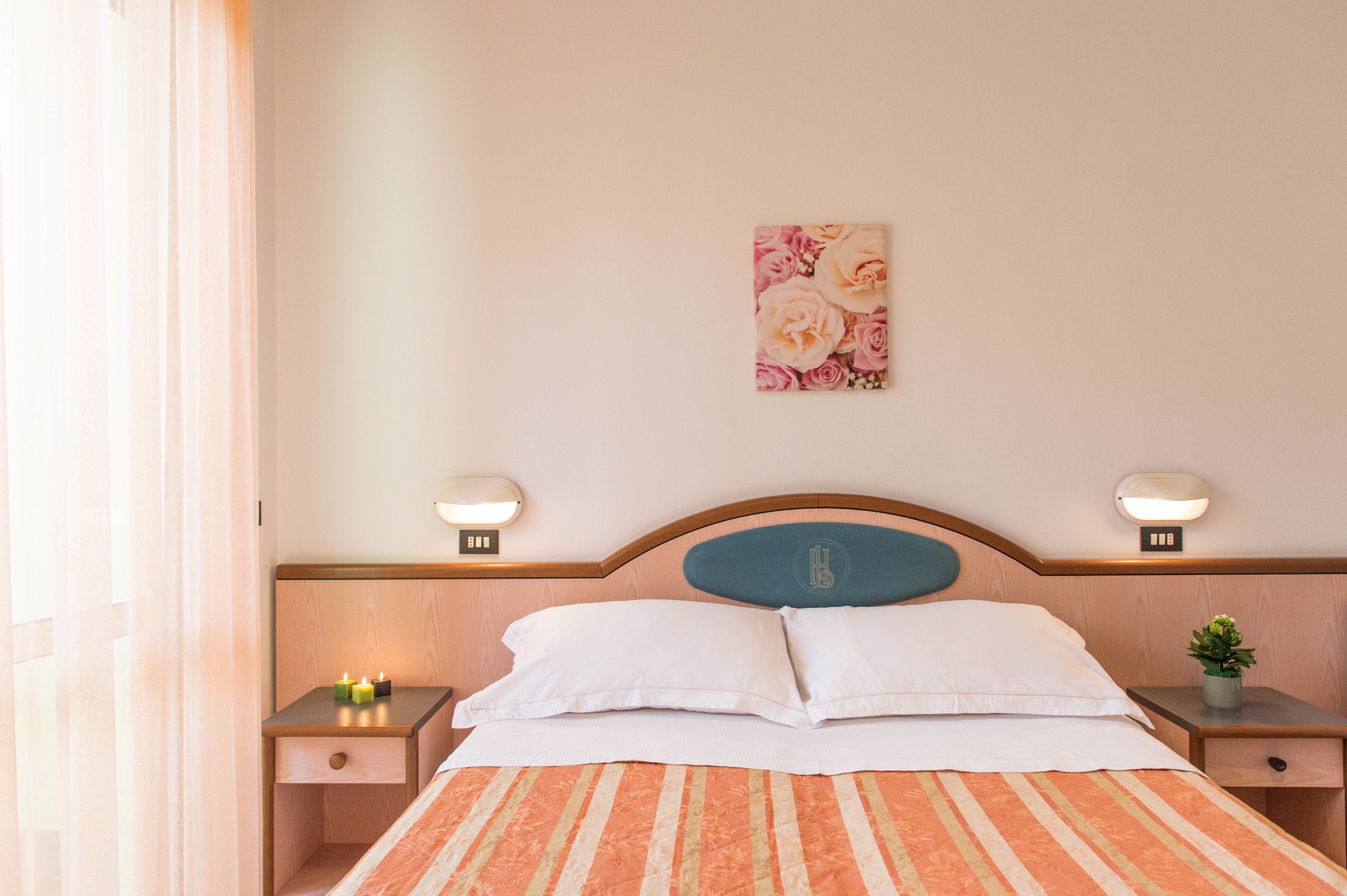 A hotel room with a bed, two bedside tables, a nightstand, a wall-mounted lamp, and a small potted plant.