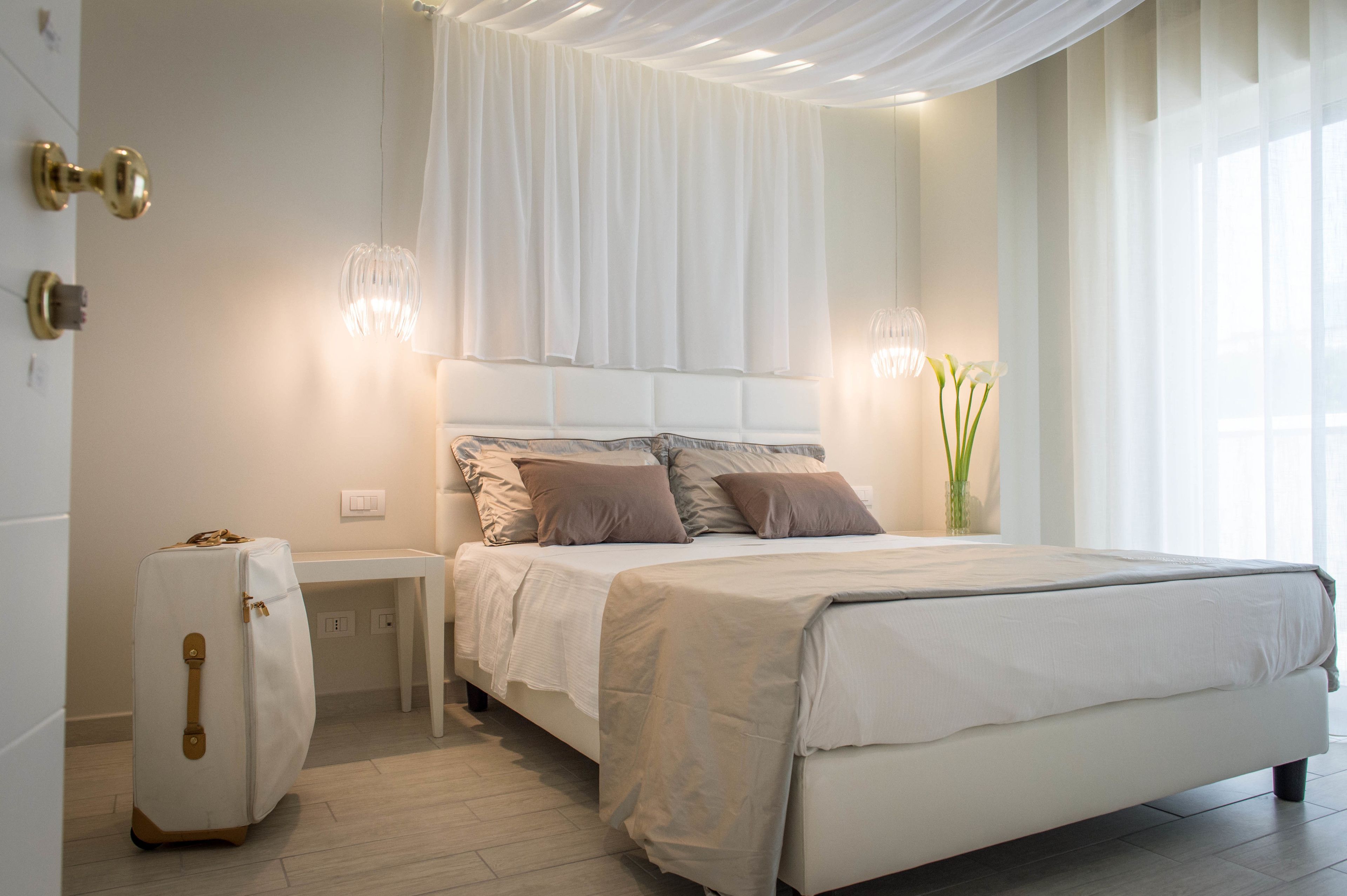 Un dormitorio moderno con una cama grande, mesitas de noche, un aparador blanco y una maleta.