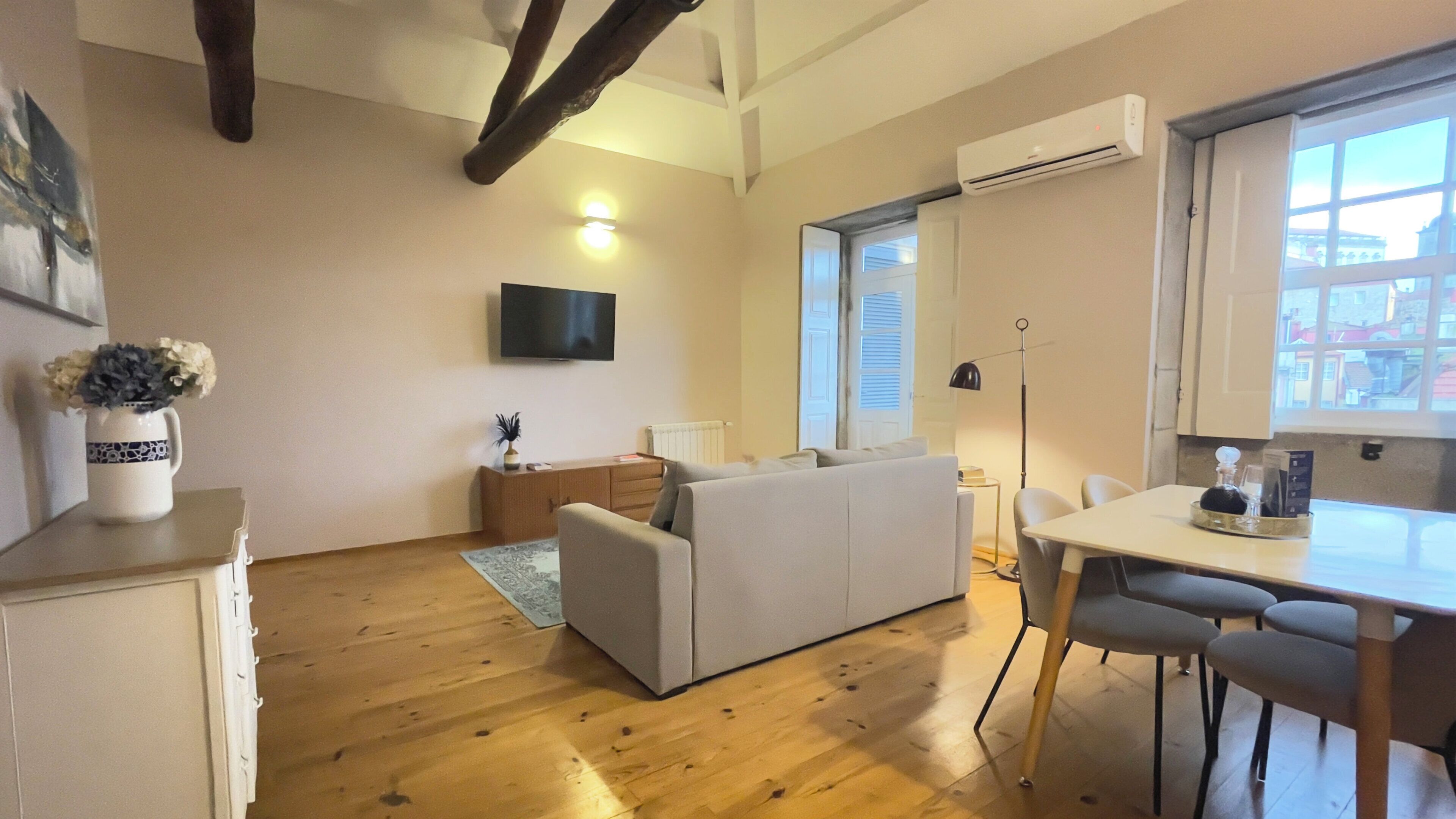 Una sala de estar moderna con un sofá, una mesa de comedor con sillas, un televisor en la pared y un equipo de aire acondicionado.