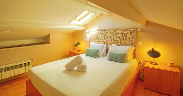 A neatly arranged bedroom with a skylight, a bed with pillows, a bedside table with a lamp, and a radiator. - FLORES 36 by YoursPorto (Porto)
