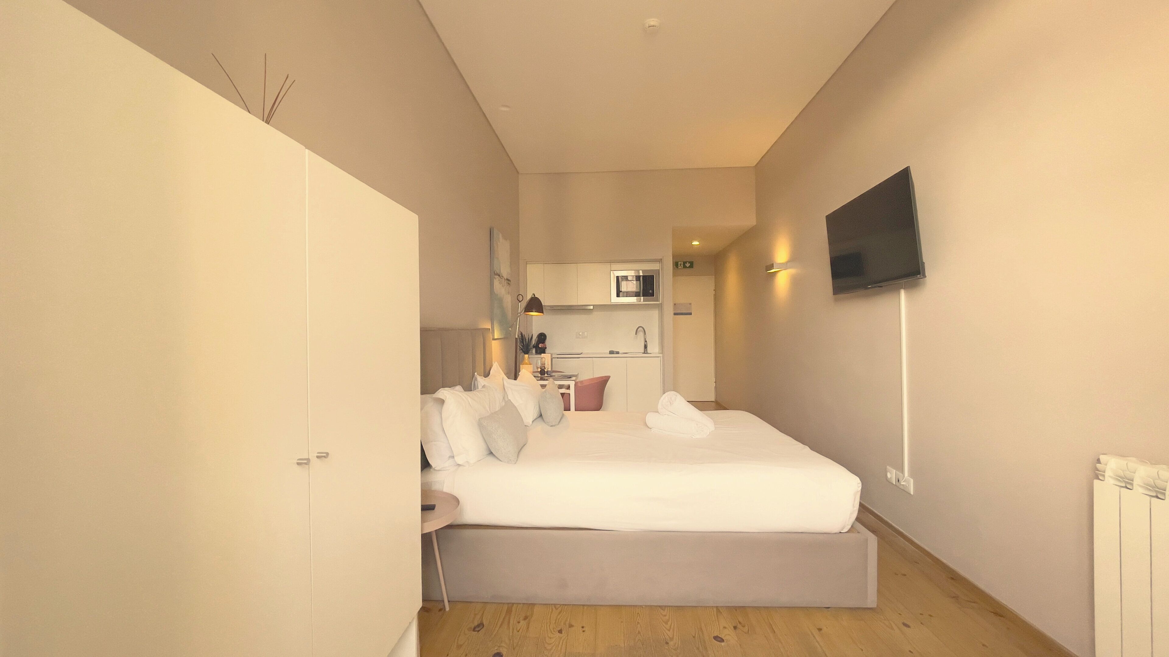 A bedroom with a bed, bedside table, and a TV mounted on the wall.