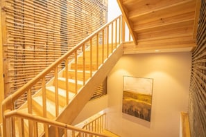 Een houten trap met een leuning, een schilderij aan de muur en een houten wand met een geweven structuur.