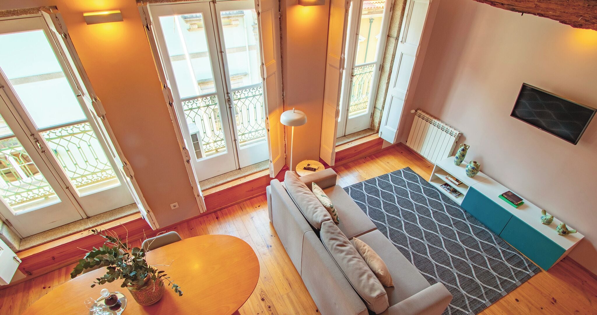 A modern living room with a sofa, a round table with a plant, and a patterned rug.