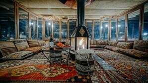 A cozy room with a large fireplace, patterned rugs, and a view of the city at night. - Elysée Cave House (Nevsehir)