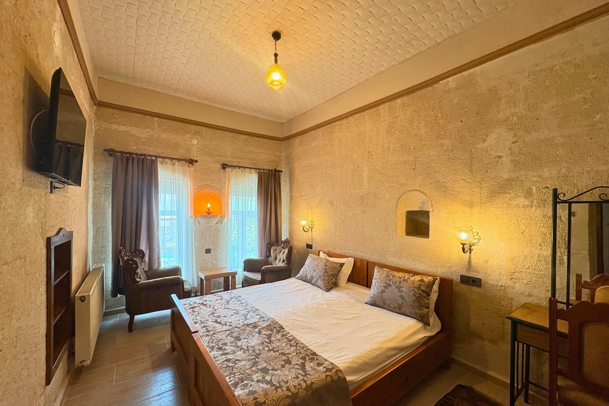 A bedroom with a large bed, a wooden bench, a small table, a TV, and a fireplace.