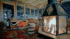 A cozy room with a large fireplace, a dining table with food and drinks, and large windows offering a view of the city at night. - Elysée Cave House (Nevsehir)