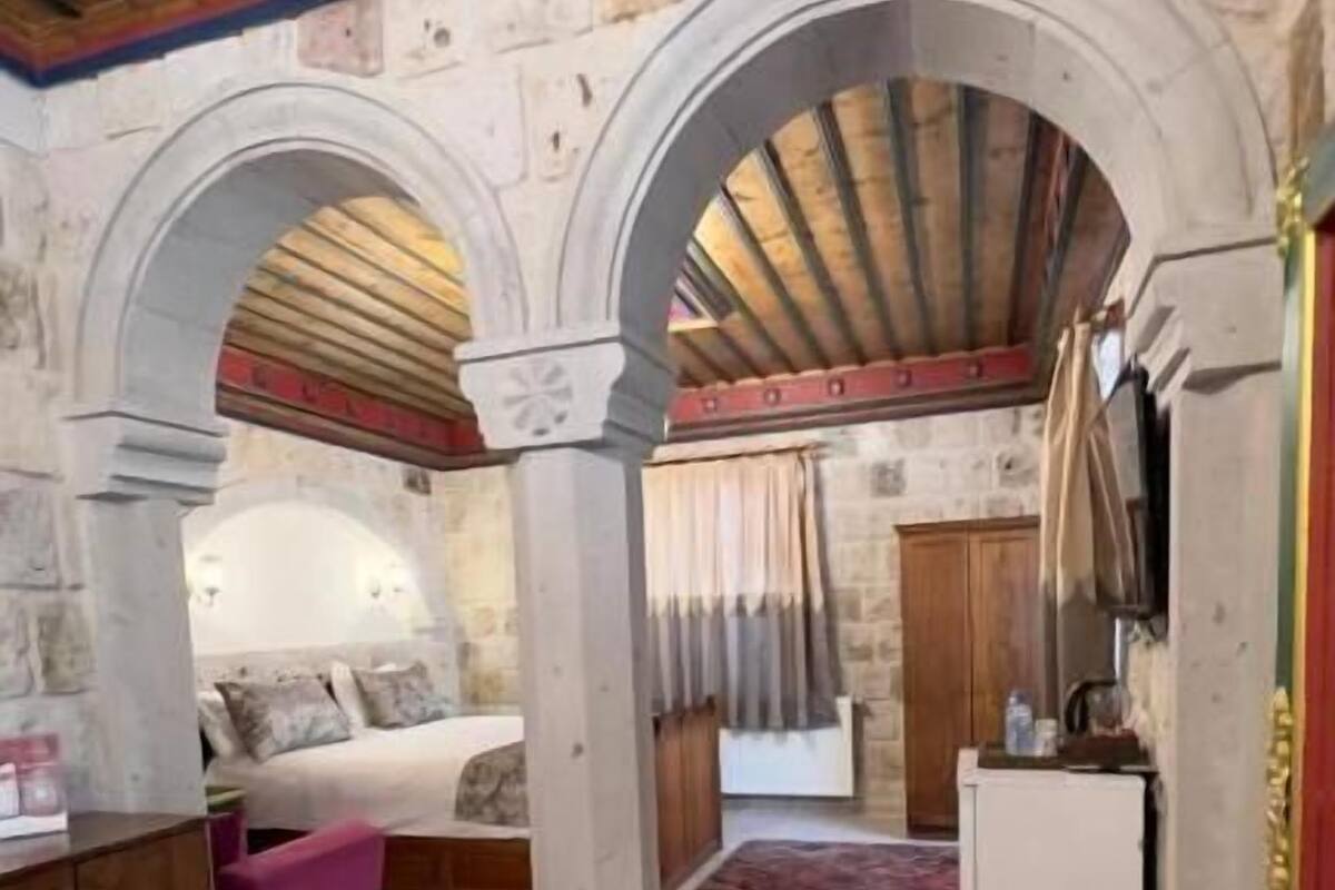A room with a bed, a small desk, a refrigerator, and a patterned rug.