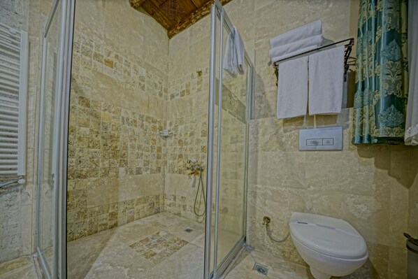 A bathroom with a glass-enclosed shower, a toilet, and a towel rack with towels. - Elysée Cave House (Nevsehir)