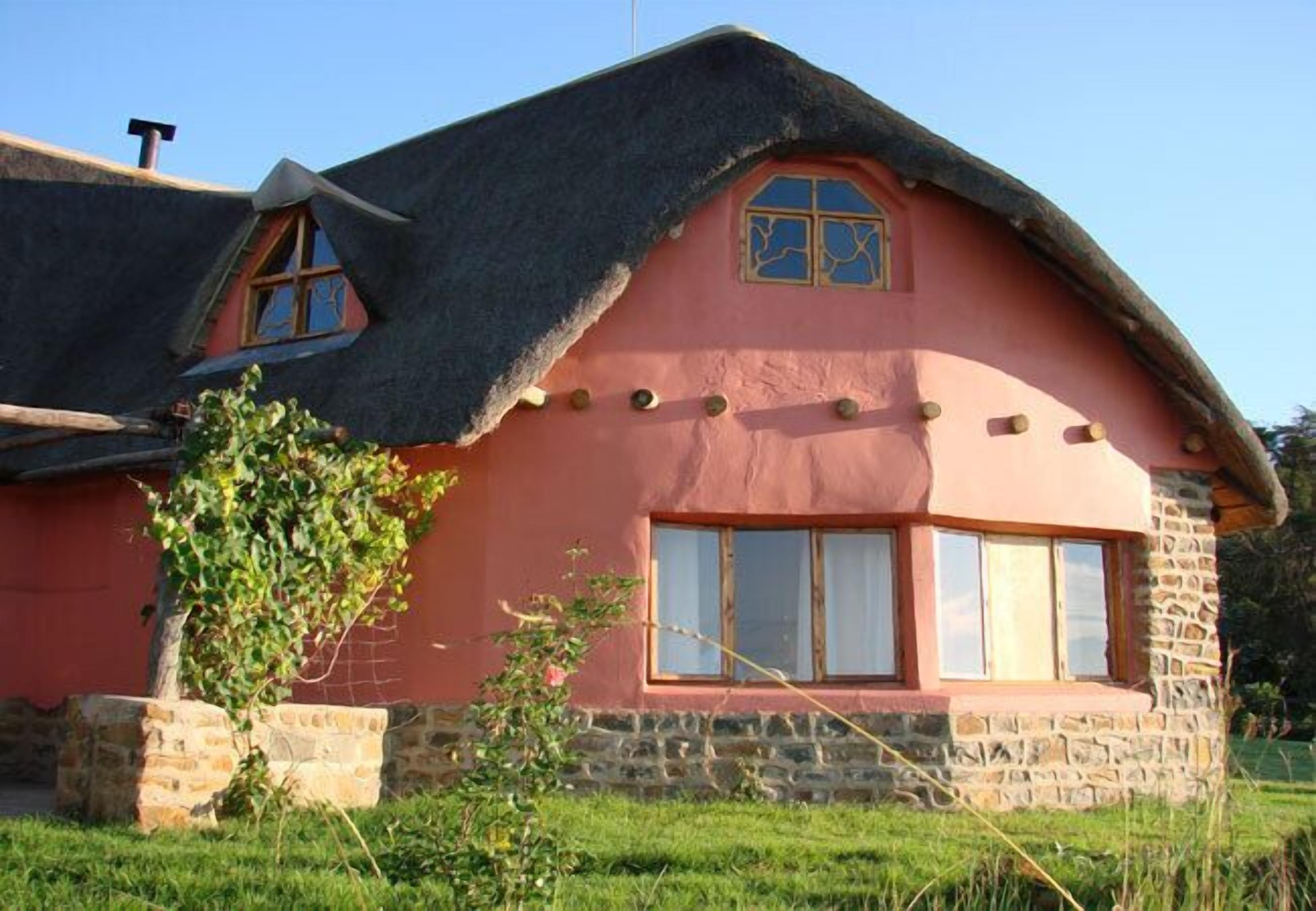 Ein Haus mit einem Strohdach, Steinmauern und einer rosafarbenen Fassade.