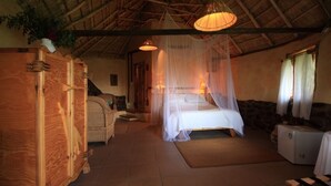 A room with a bed under a canopy, a wooden cabinet, a small table, and a refrigerator.