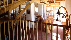A rustic wooden interior with a dining area, wooden staircase, and a view of the outdoors.
