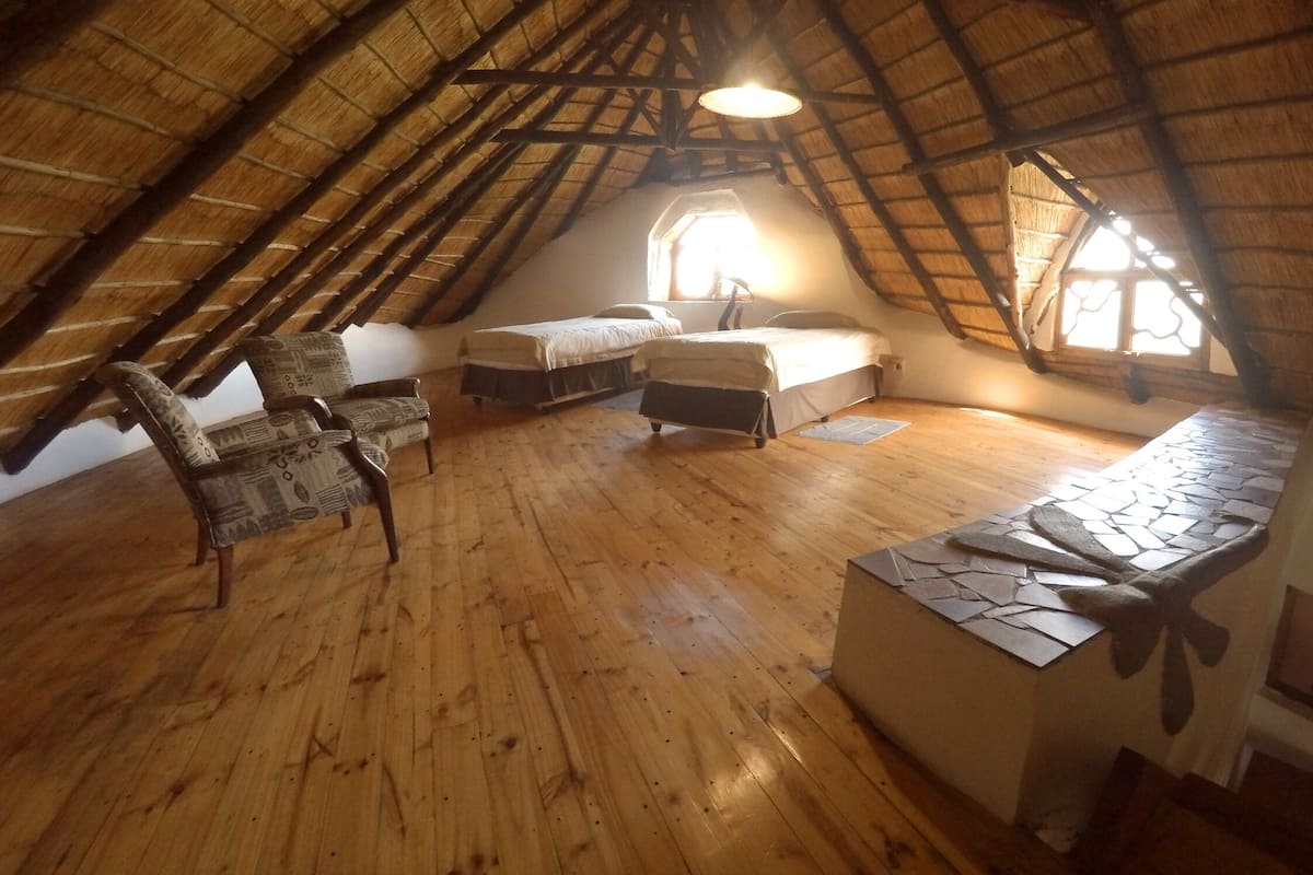 Een gezellige slaapkamer op zolder met een schuine kap, houten vloeren, twee bedden, een stoel en een kleine tafel.