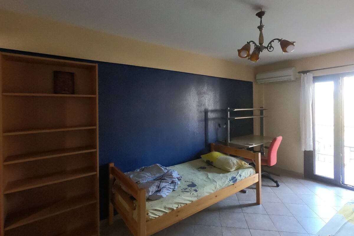 A room with a bunk bed, a wooden wardrobe, a desk, and a chair.