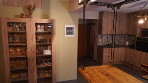 A kitchen with wooden cabinets, a wooden table, and a hanging light fixture. - Arabas - Hostel (Thessaloniki)