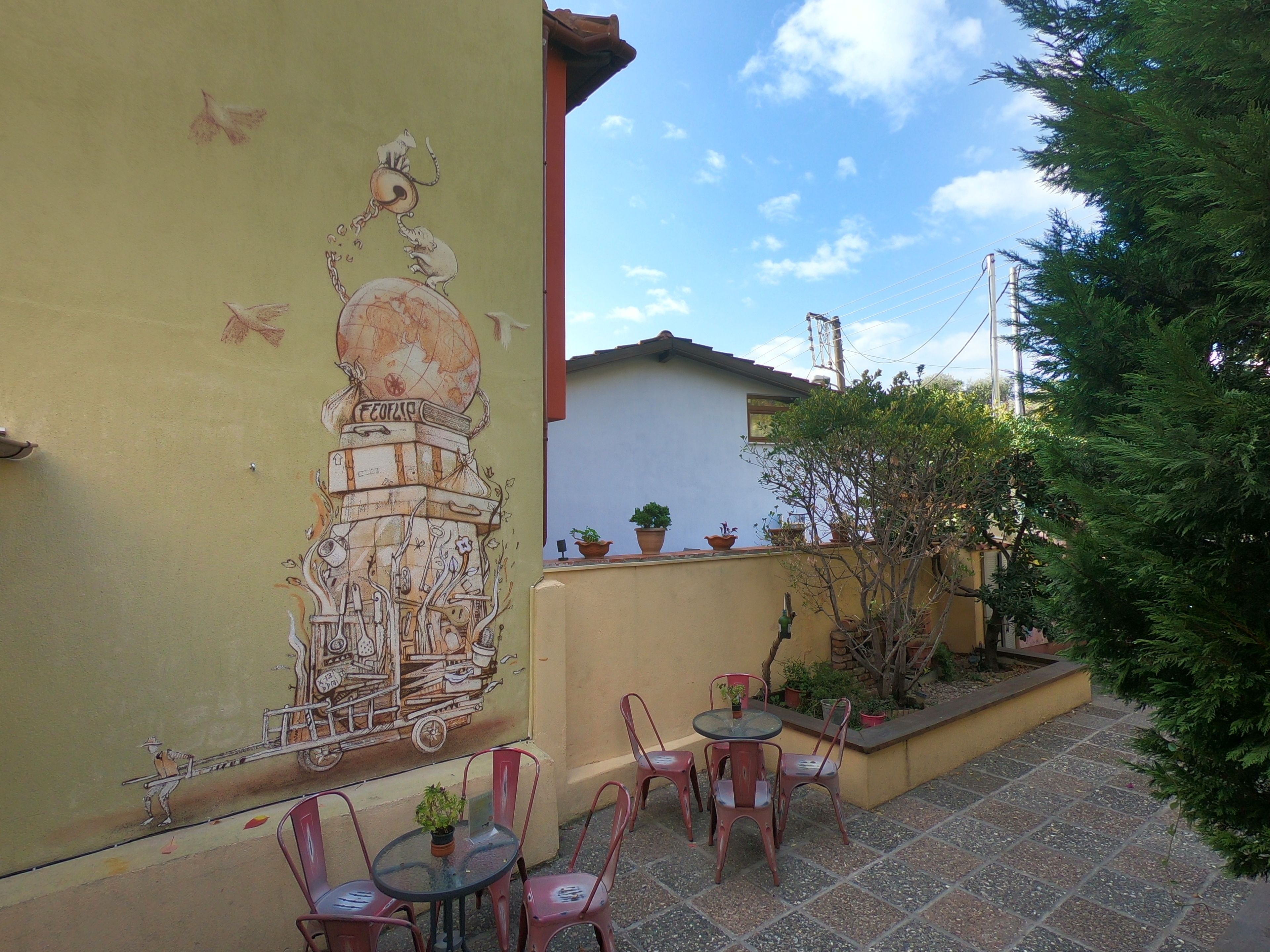 Un patio con un mural, asientos al aire libre y plantas en macetas.