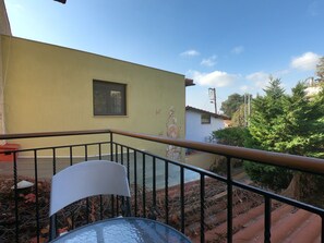 Un balcón con barandilla de metal, una silla blanca y una mesa de vidrio.