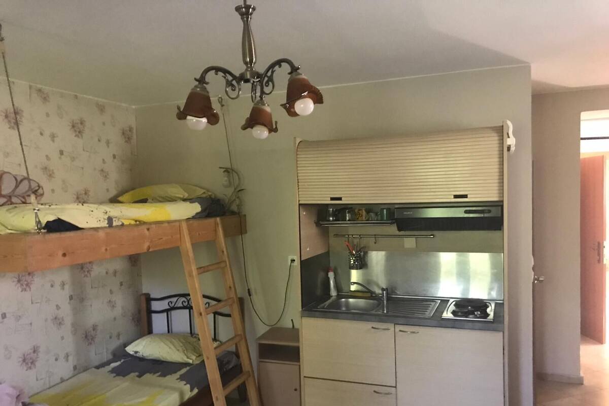 A compact room with a bunk bed, a kitchenette with a stove and sink, and a ceiling light fixture.