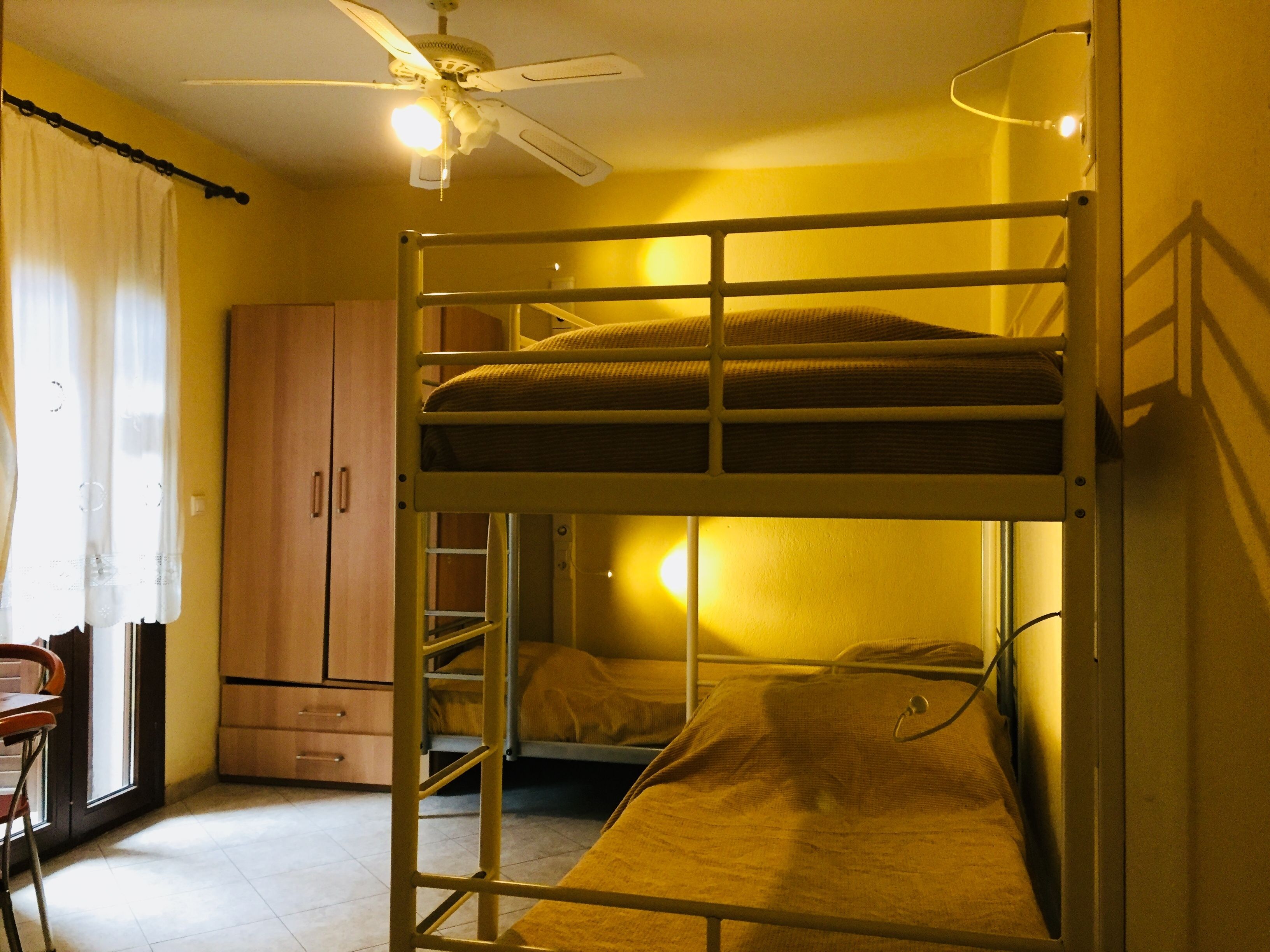 Um dormitório com beliches, ventilador de teto, armário de madeira e uma escrivaninha com cadeira.