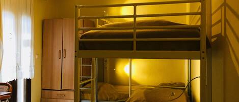 Une chambre de dortoir avec des lits superposés, un ventilateur de plafond, une armoire en bois et un bureau avec une chaise.