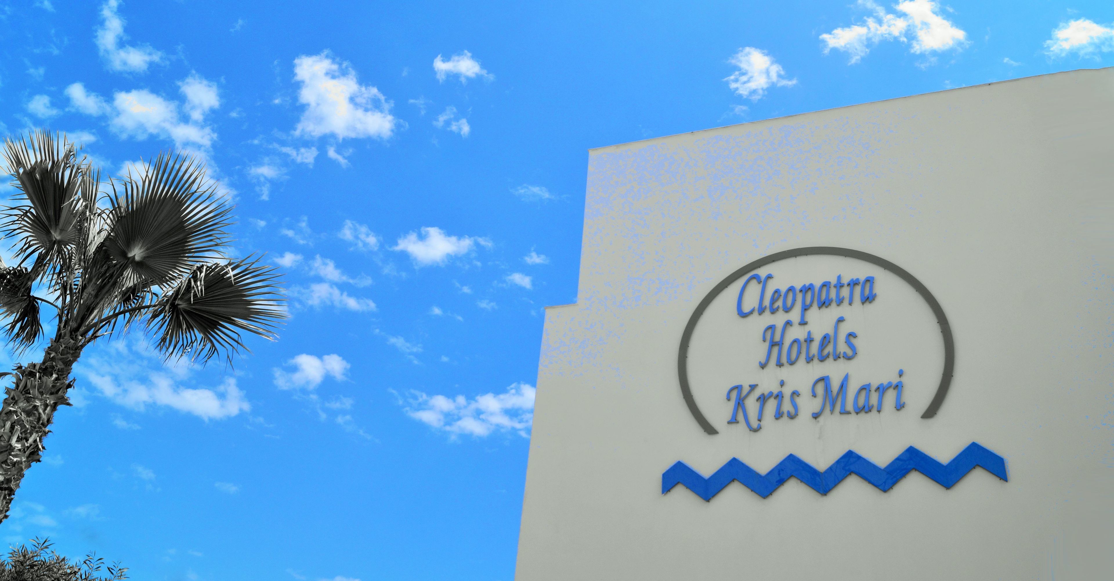 A hotel sign with the name "Cleopatra Hotels Kris Mari" against a clear blue sky.