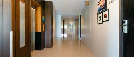 Un pasillo moderno de hotel con paneles de madera, suelo de baldosas limpias y cuadros en las paredes.