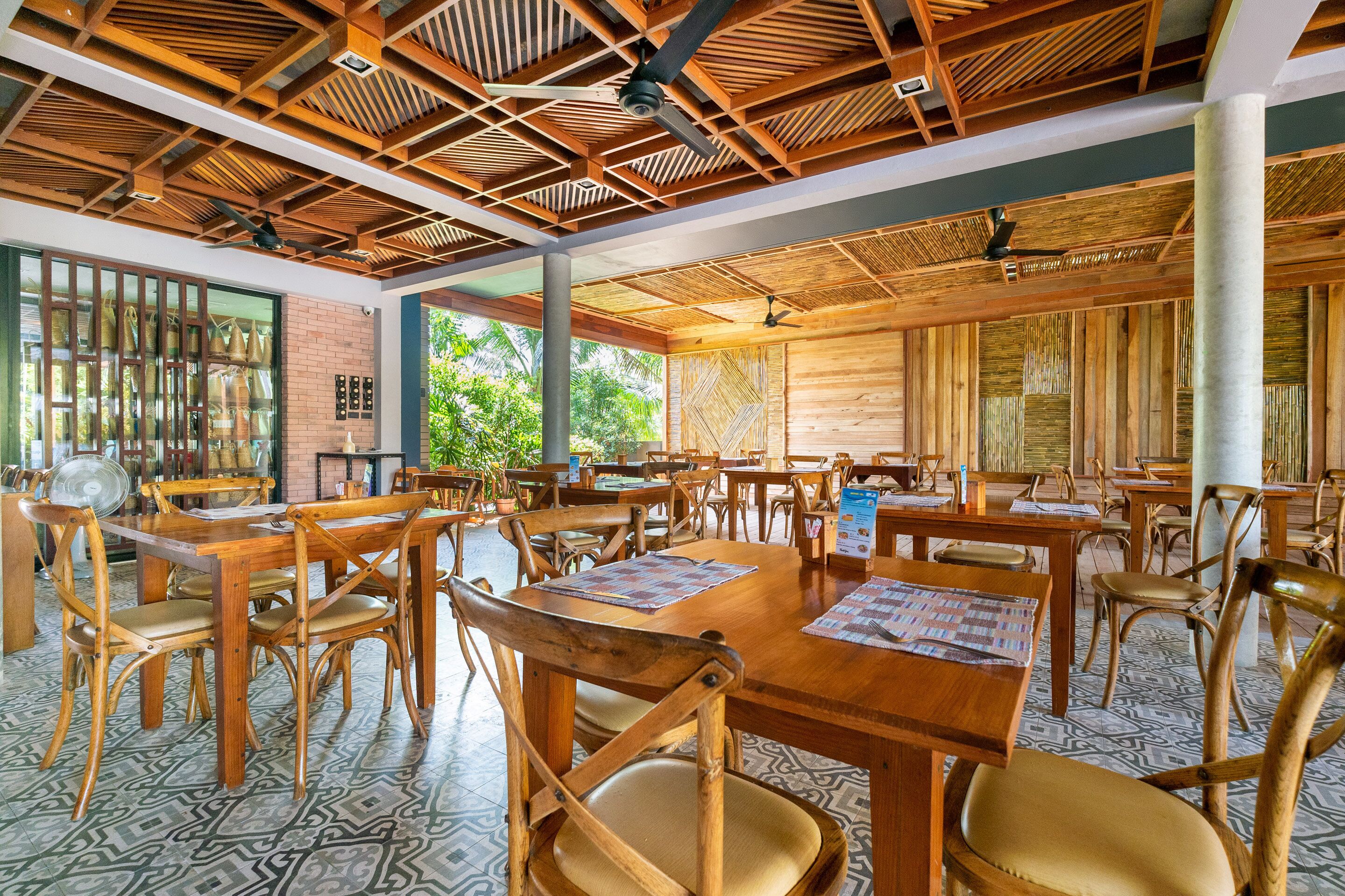 A spacious dining area with wooden tables and chairs, large windows, and a patterned floor.