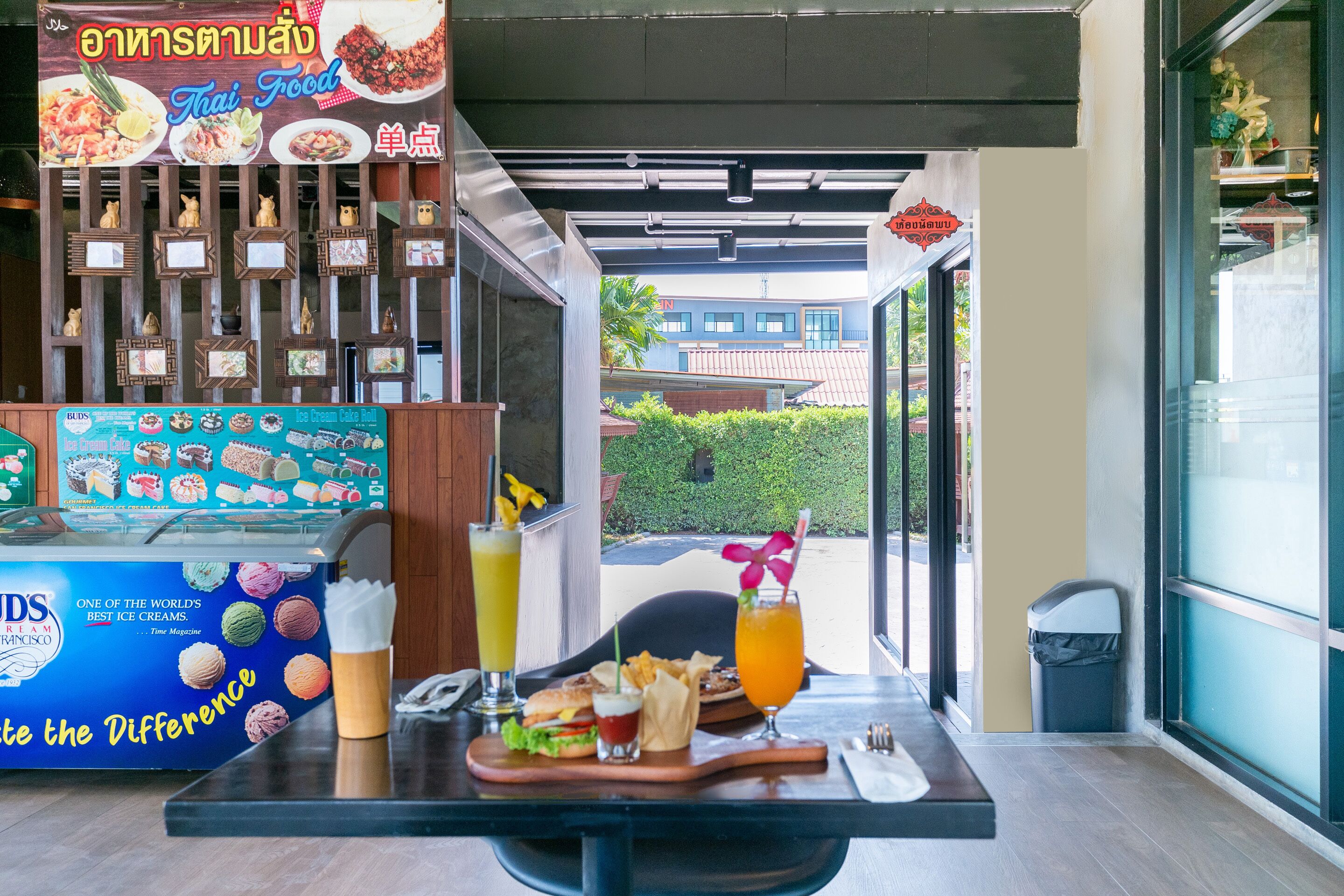 A Thai food restaurant with a menu board, ice cream display, and a table set with food and drinks.