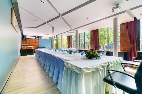 A conference room with long tables, a wooden counter, and large windows with curtains.
