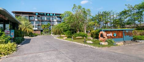 A hotel entrance with a clear pathway, a sign for 'The Tama Hotel', and surrounding greenery.