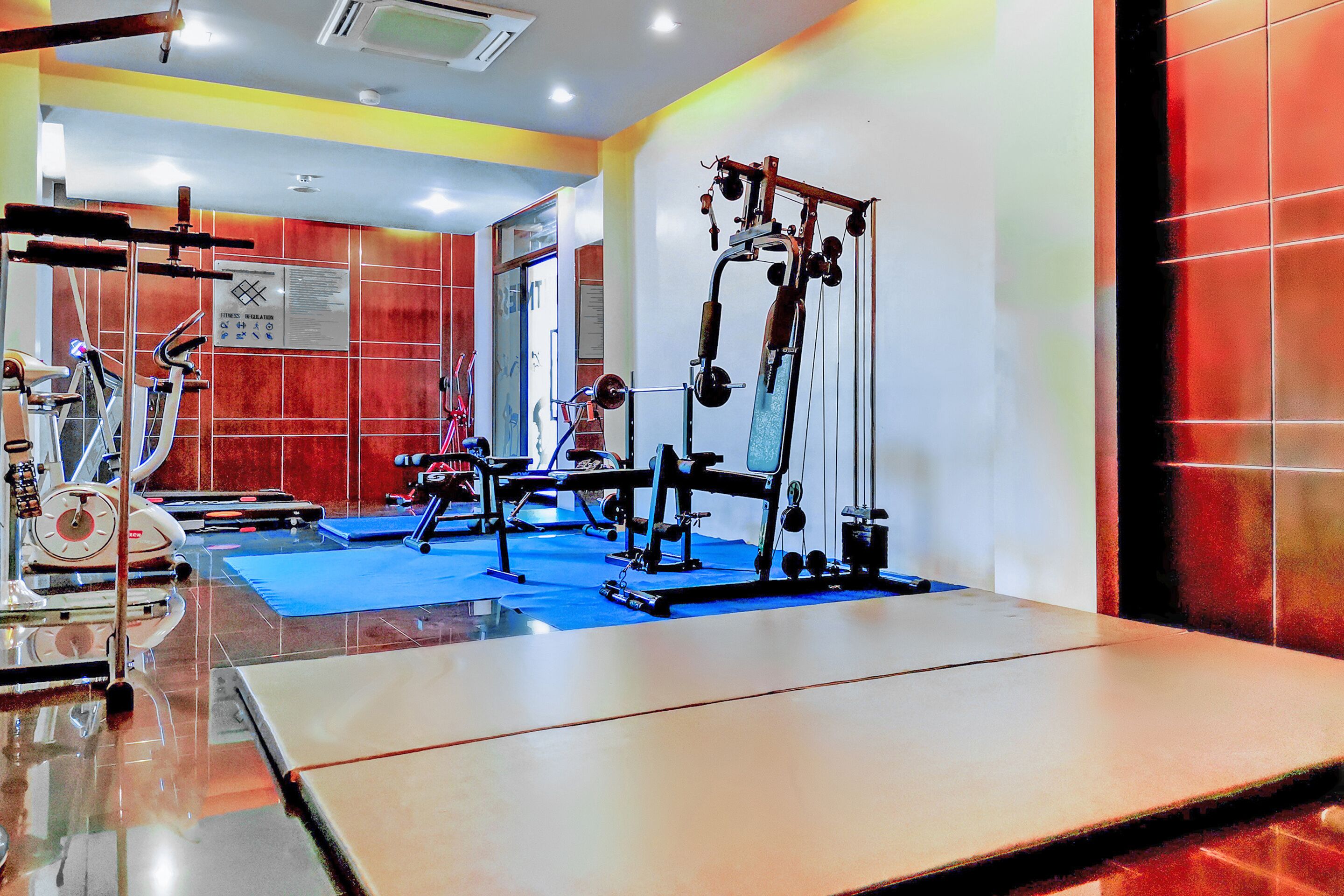 Un gimnasio con varios equipos de ejercicio, una colchoneta azul y un espejo grande.