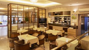 Un restaurant amb diverses taules i caires, una zona de bar i una cuina visible a través d'un panell de vidre.