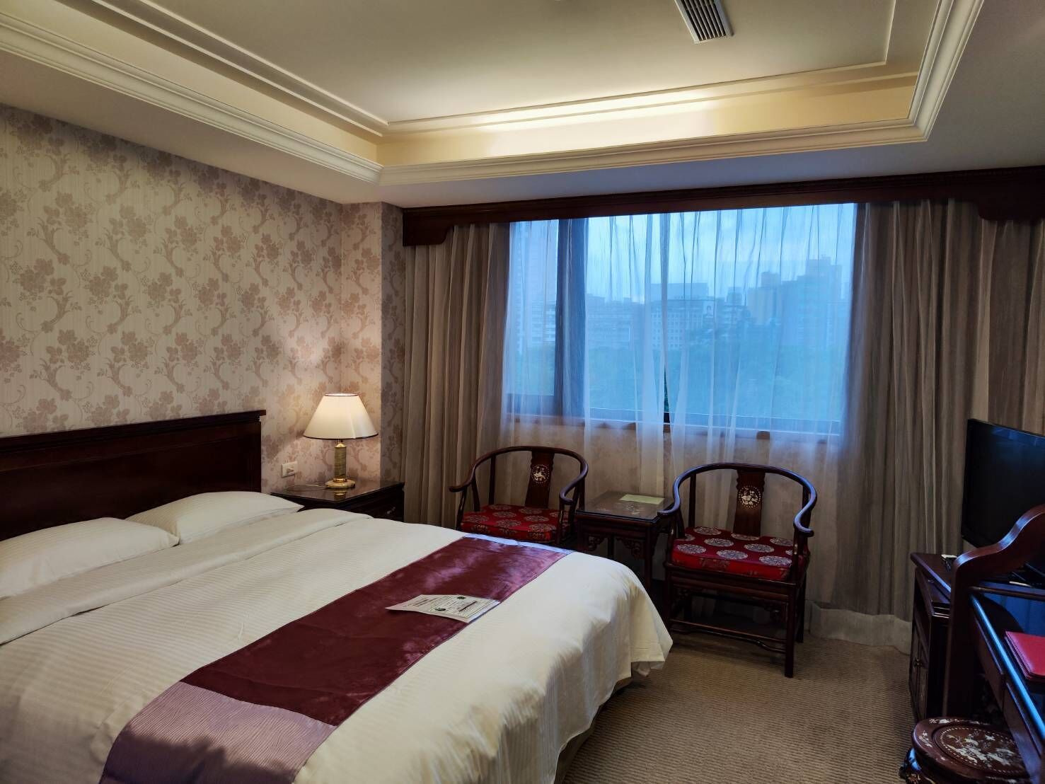 Una habitación de hotel con una cama grande, dos sillones, un escritorio, una lámpara y un televisor.