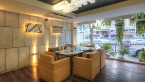 A modern interior with a dining area featuring wicker furniture and a view of the street through large windows.