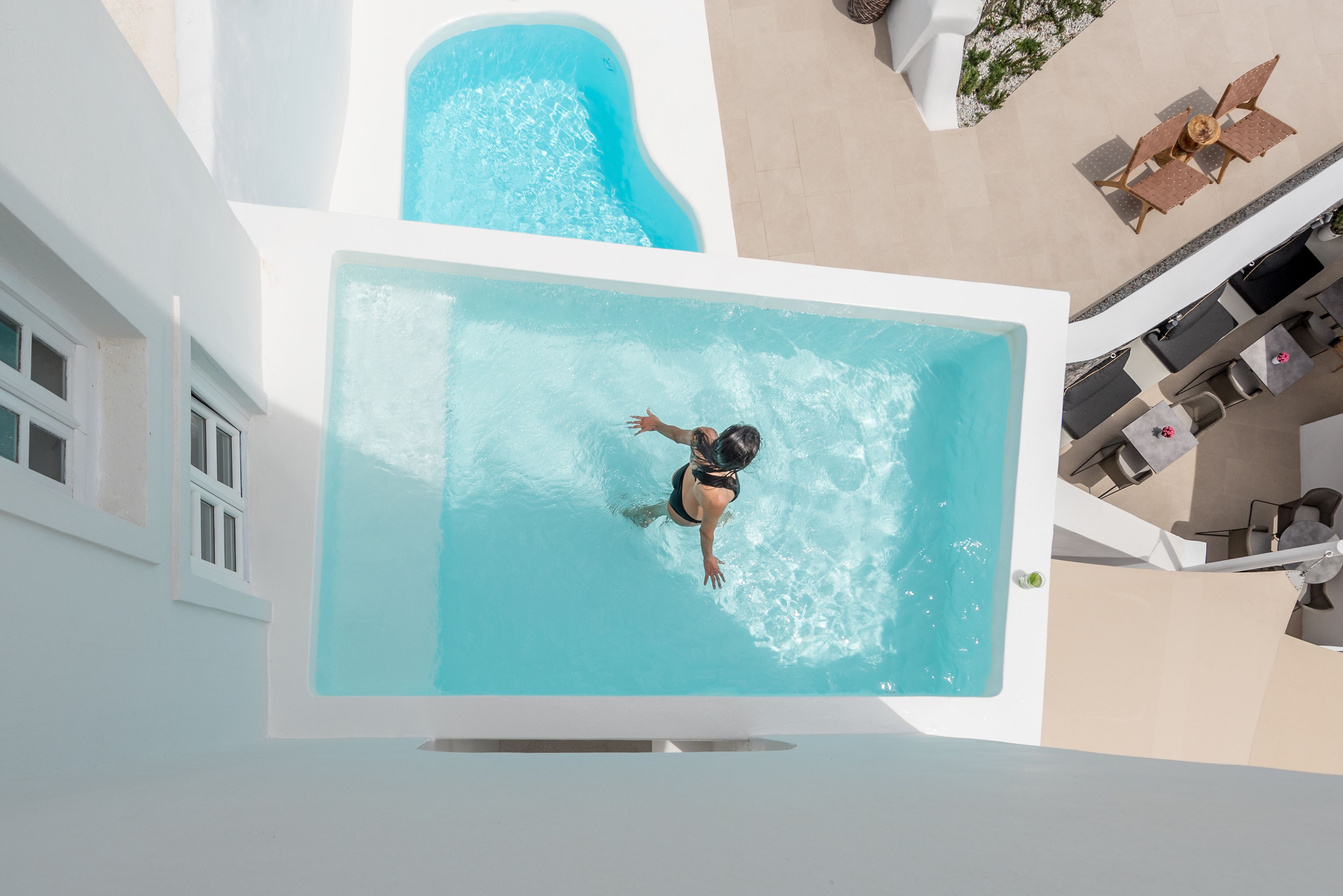 A rooftop swimming pool with a person swimming, surrounded by outdoor seating and a white building.