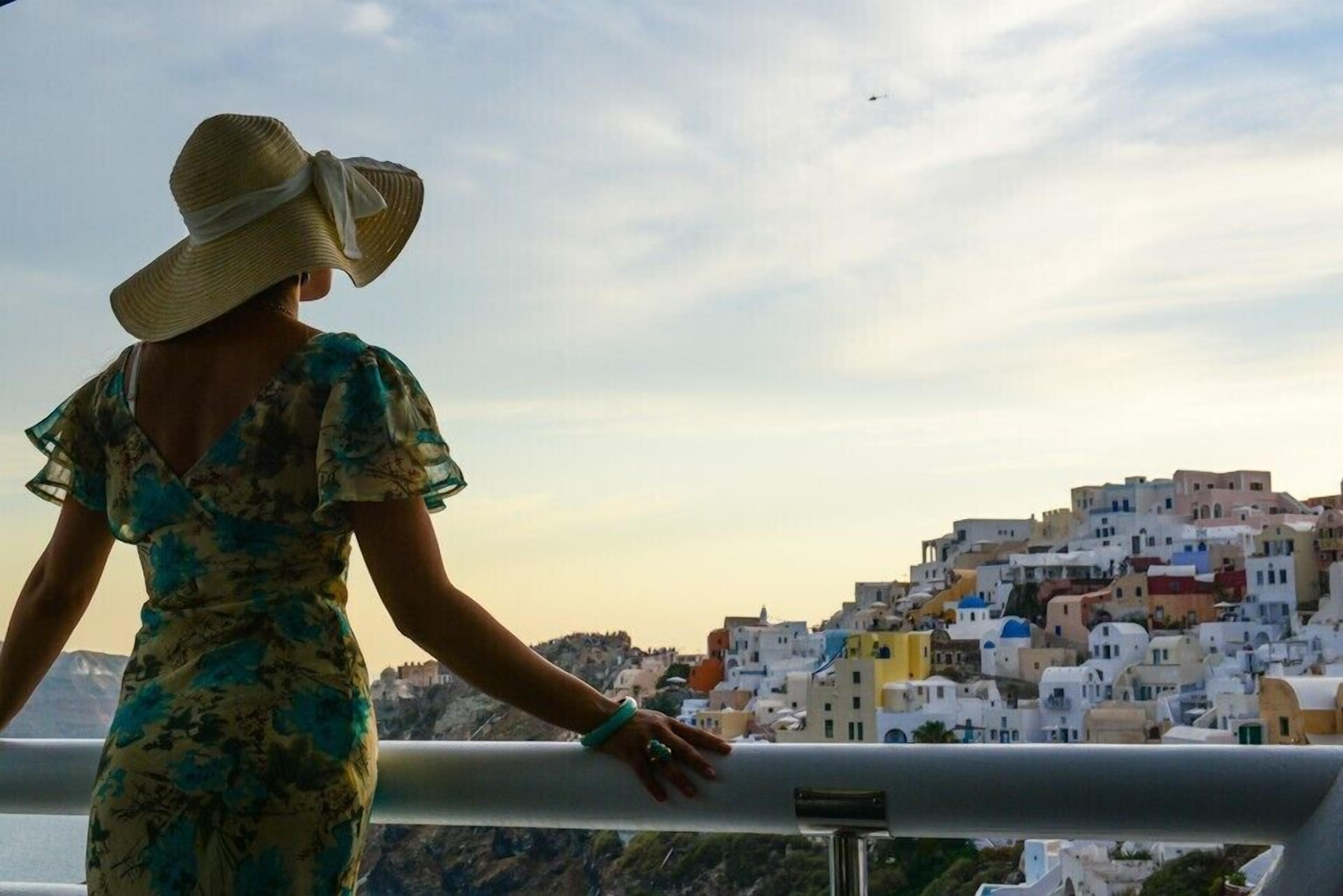 Una persona con vestido y sombrero contempla un paisaje con edificios de colores en una colina.