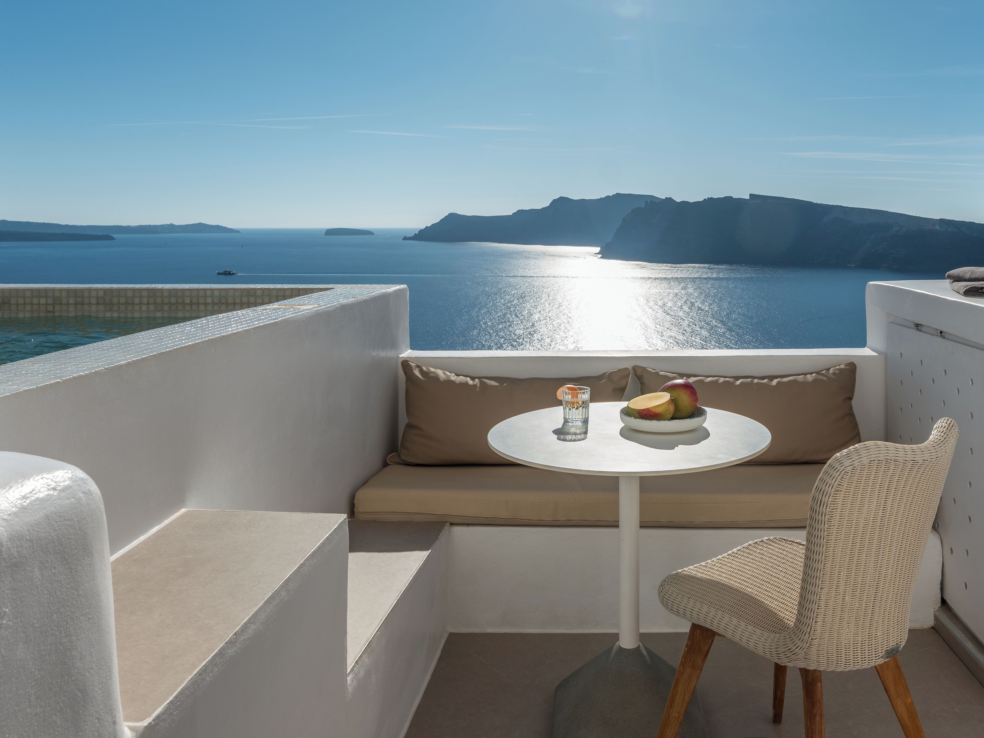 A balcony with a white table, a wicker chair, and a bowl of fruit.