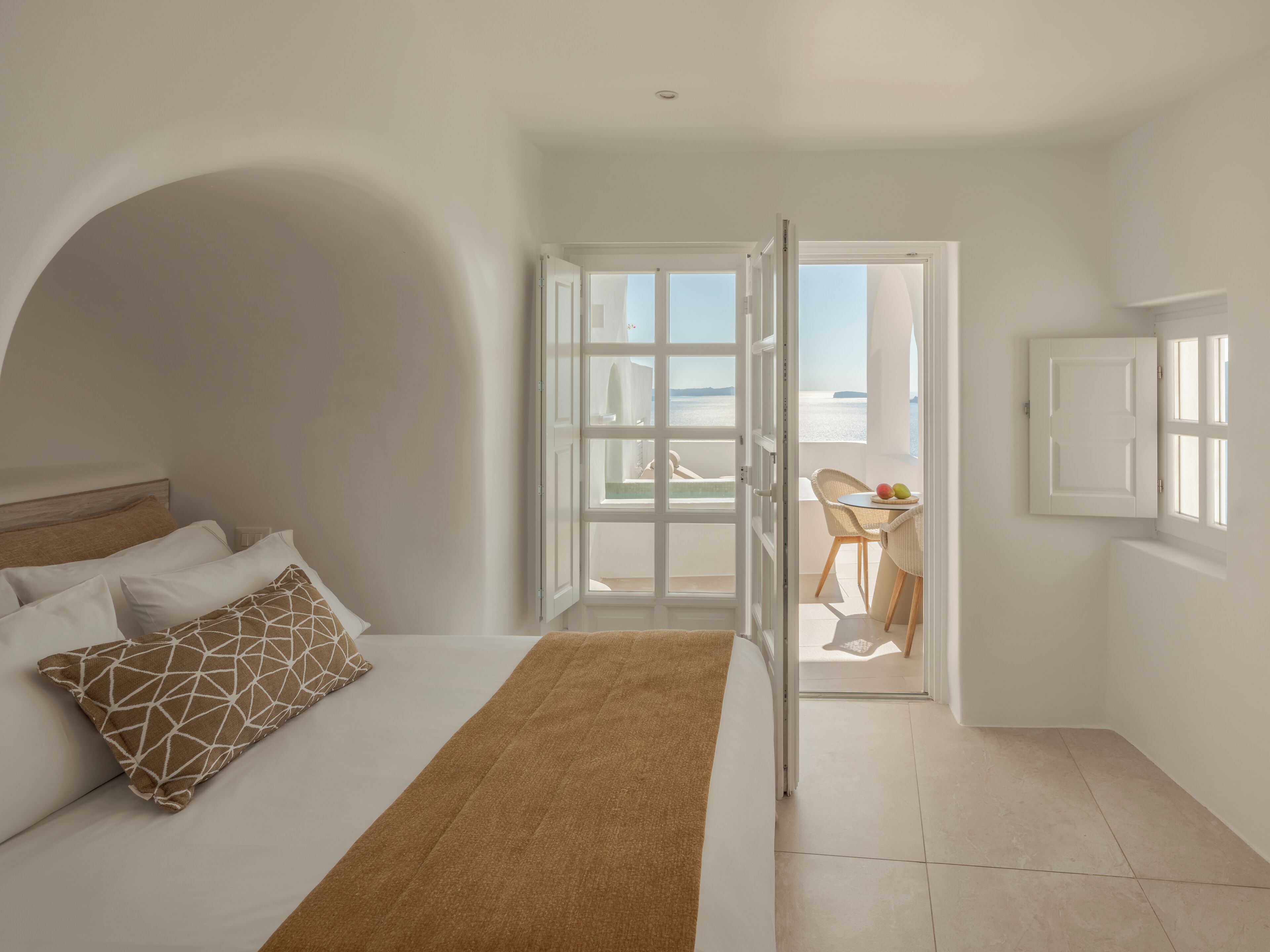 Un dormitorio con una cama, un tapete marrón y vista al mar a través de una puerta abierta.