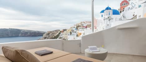 A balcony with a view of a coastal town, a sofa, and a small table with a book and a glass.